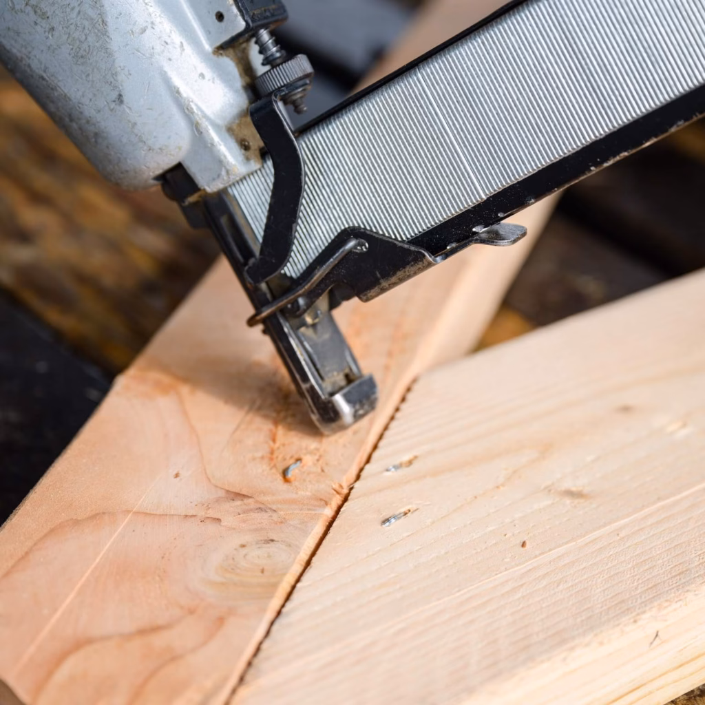 a nail gun nailing the corner of two pieces of wood during the building of a roof truss system